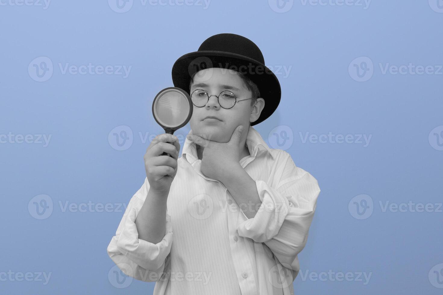 Young detective. Black and white retro portrait of a boy in 1920s clothes. Bowler hat, white shirt and magnifying glass. Art mix with blue background photo