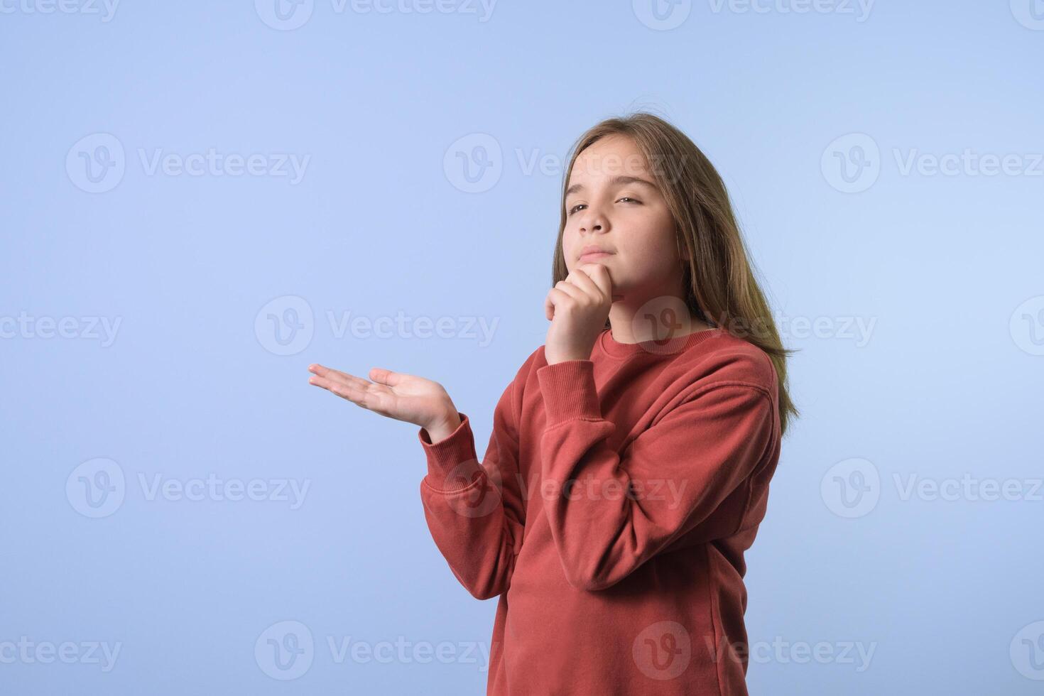The girl is dreaming about something, her hand is raised for the object showing a copy space on her palm for advertising . Blue background, red sweater photo