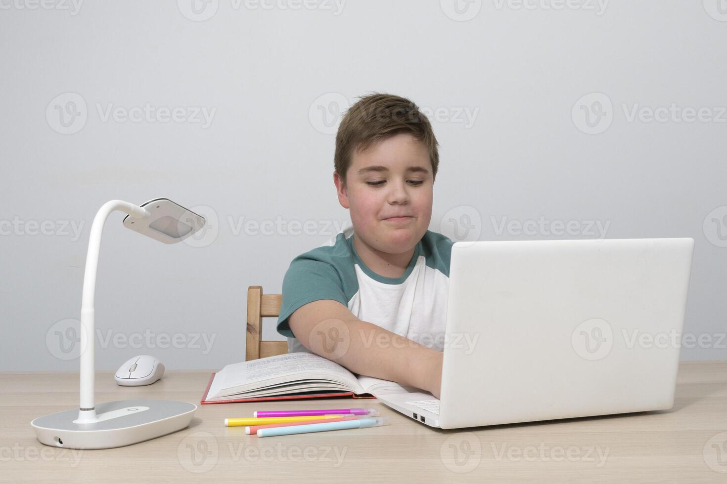 Boy teenager with a computer at the table. Typing on the keyboard with positive emotion photo