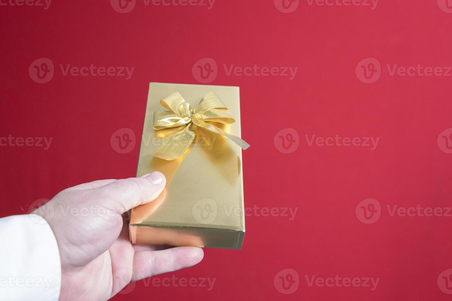 A beautiful gift in a golden package in a man's hand with a bow. on a red background close-up. place for text photo