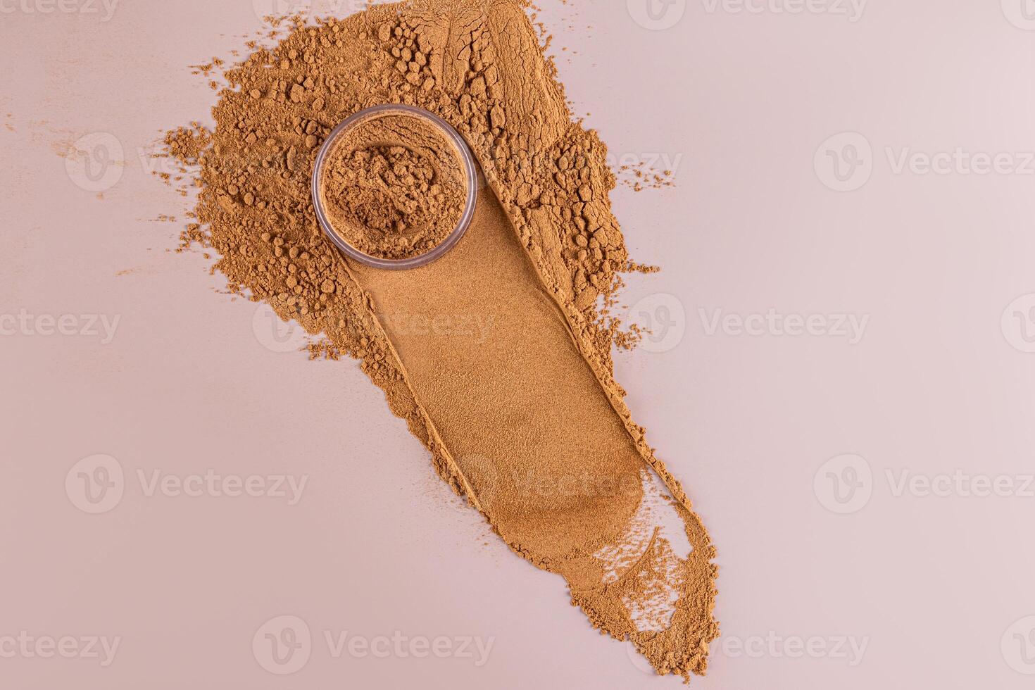A cosmetic jar with loose powder in a bronzer tone stands on the sample with a trace of a jar and a background of loose powder. decorative cosmetics. photo
