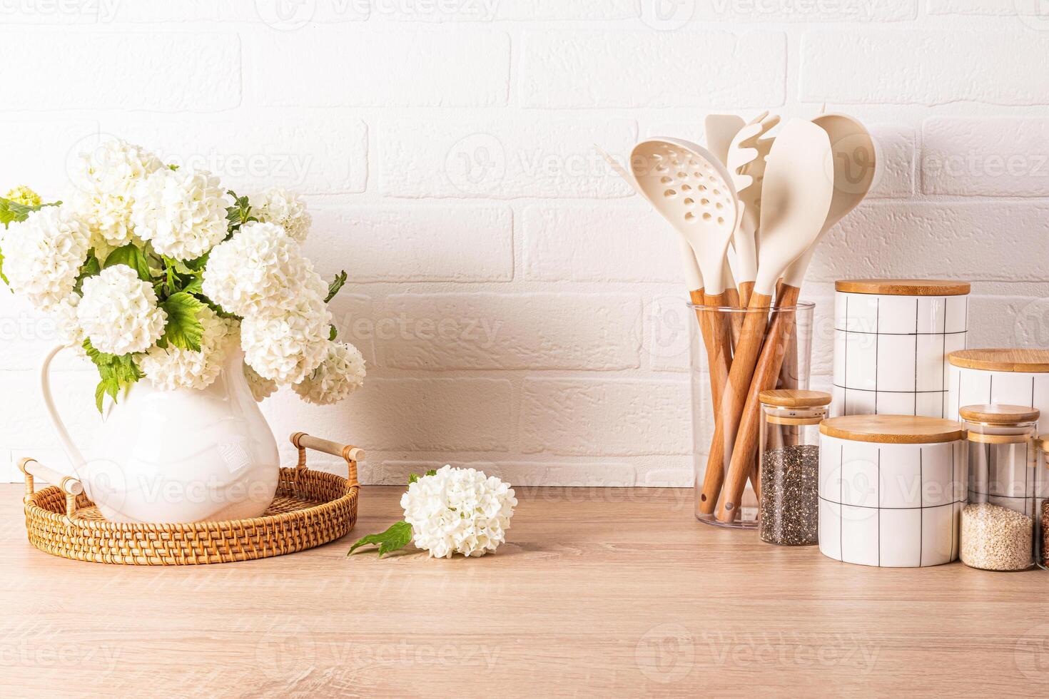 A set of tools for cooking food in a stand, a set of white ceramic jars, a jug with flowering branches in a wooden countertop. Eco style. photo