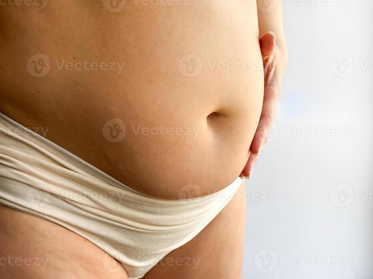Pregnant belly in beige underwear with hand touching. Close up photography for maternity, pregnancy, and motherhood concept. Design for healthcare, prenatal care and wellness. photo