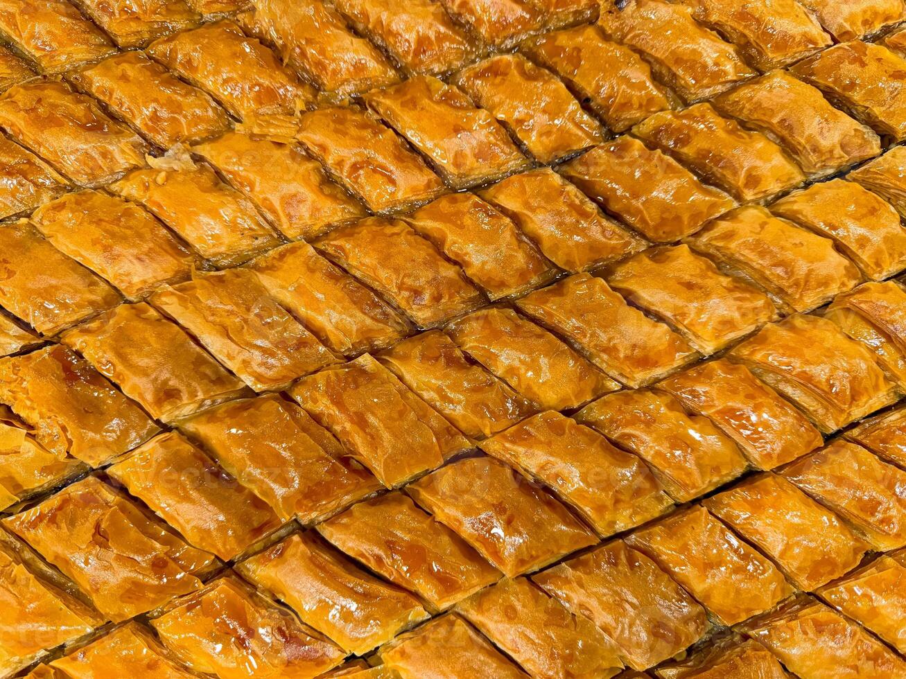 Solid background of freshly baked baklava laid out in rows, golden brown with syrup glaze, traditional Middle Eastern sweet pastry dessert, close up texture. Ramadan concept. photo