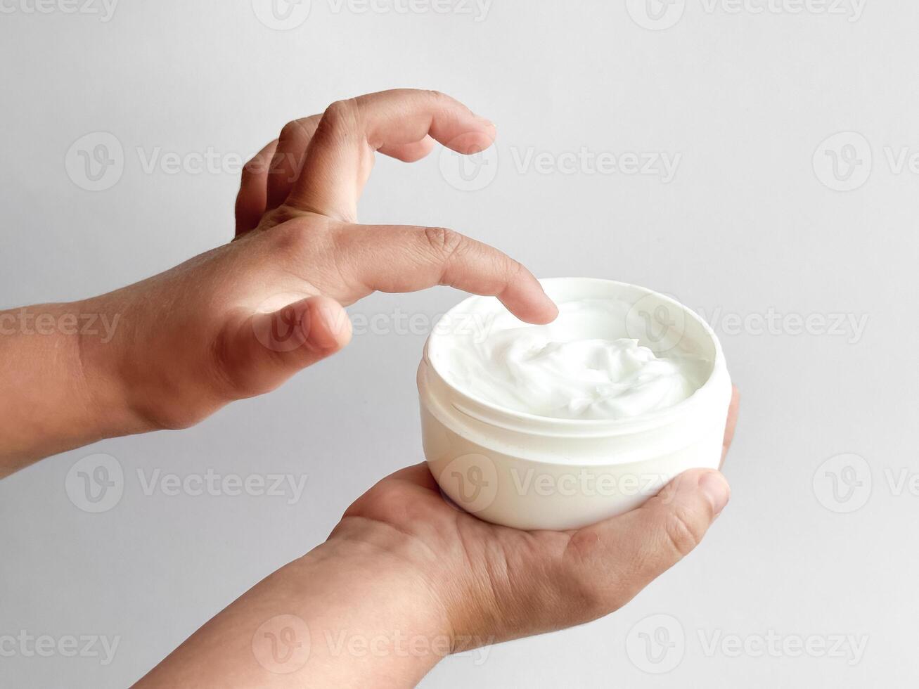 Close up of childs hands holding container of hand cream and dipping finger on white background. Skincare and moisturizing concept. Design for healthcare, wellness, and child care poster. photo