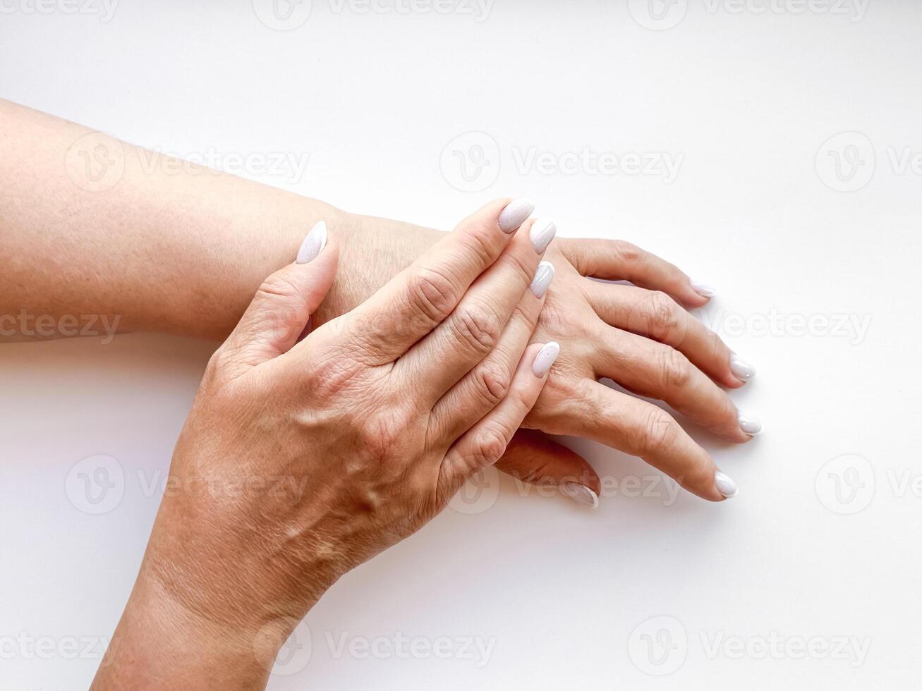 Hands middle age woman with white manicured nails gently touching each other on white background, top view. Flat lay composition. Skincare and hand care or mother love concept. photo