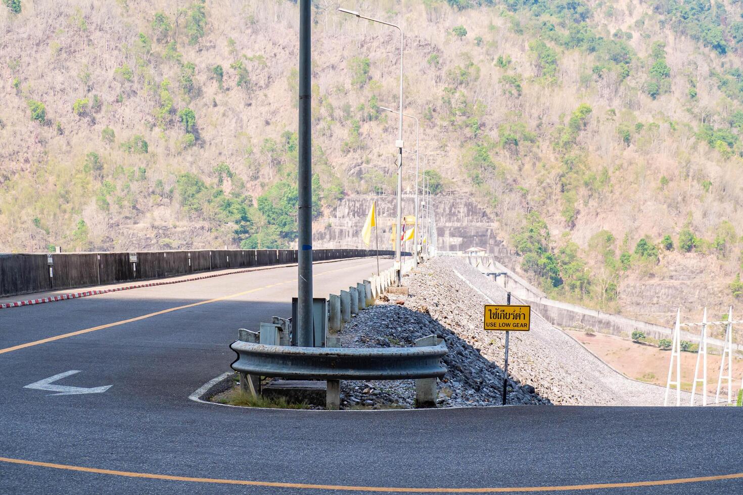 The scene of the road at the top of the dam, with the mountains in the background and a light pole. photo