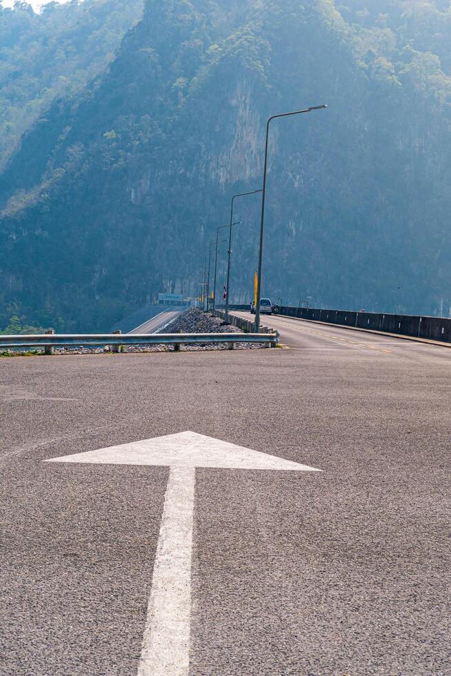 The scene of the road at the top of the dam, with the mountains in the background and a light pole. photo