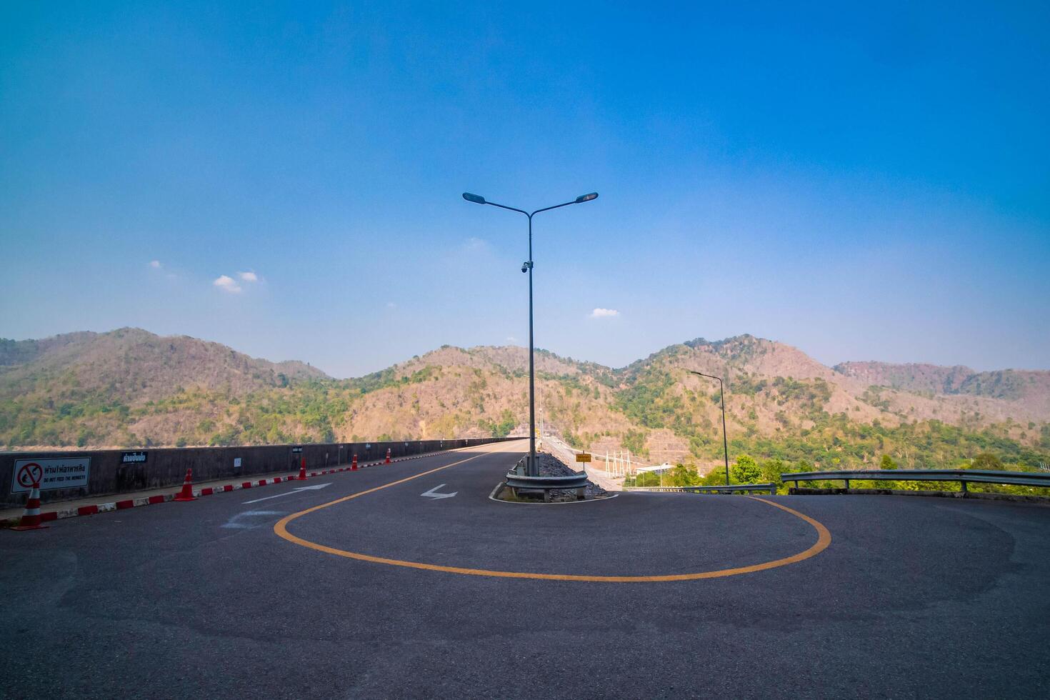 The scene of the road at the top of the dam, with the mountains in the background and a light pole. photo