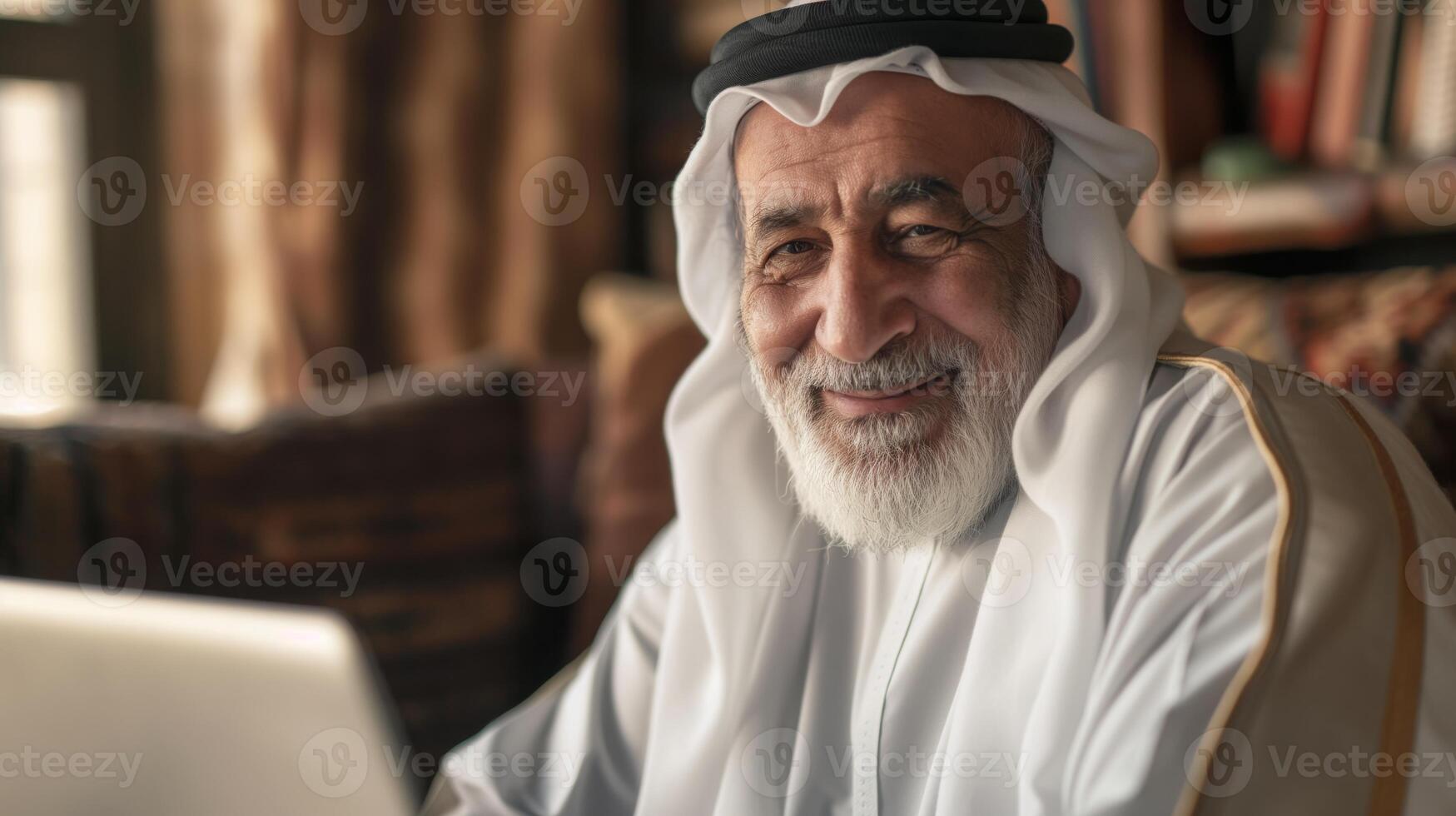 Portrait of a Smiling Elderly Middle Eastern Man in Traditional Attire, Seated at a Desk with Books in the Background photo