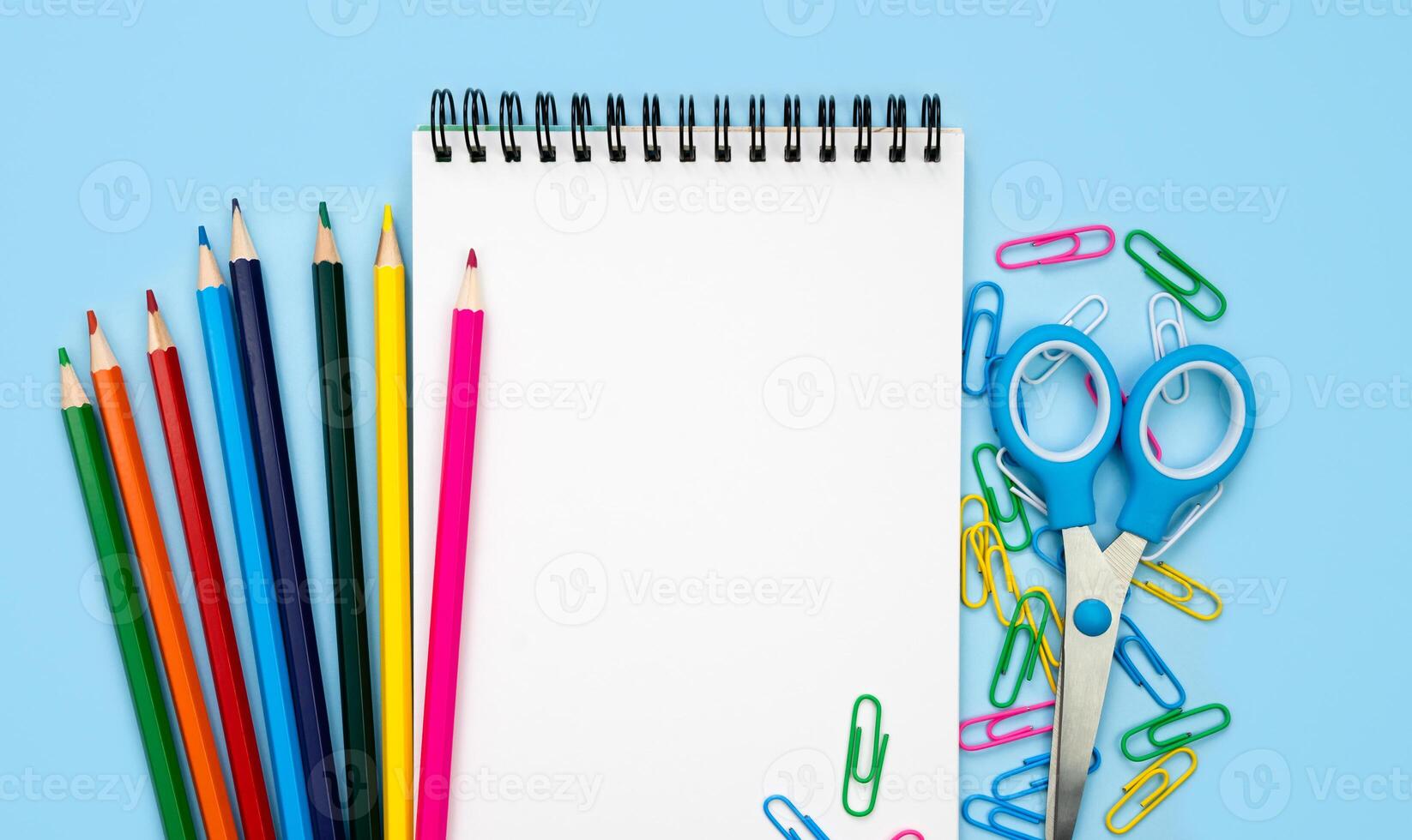 A white blank notebook and colorful school stationery on a blue background. Mockup. Flatlay. Top view. Copy space. photo