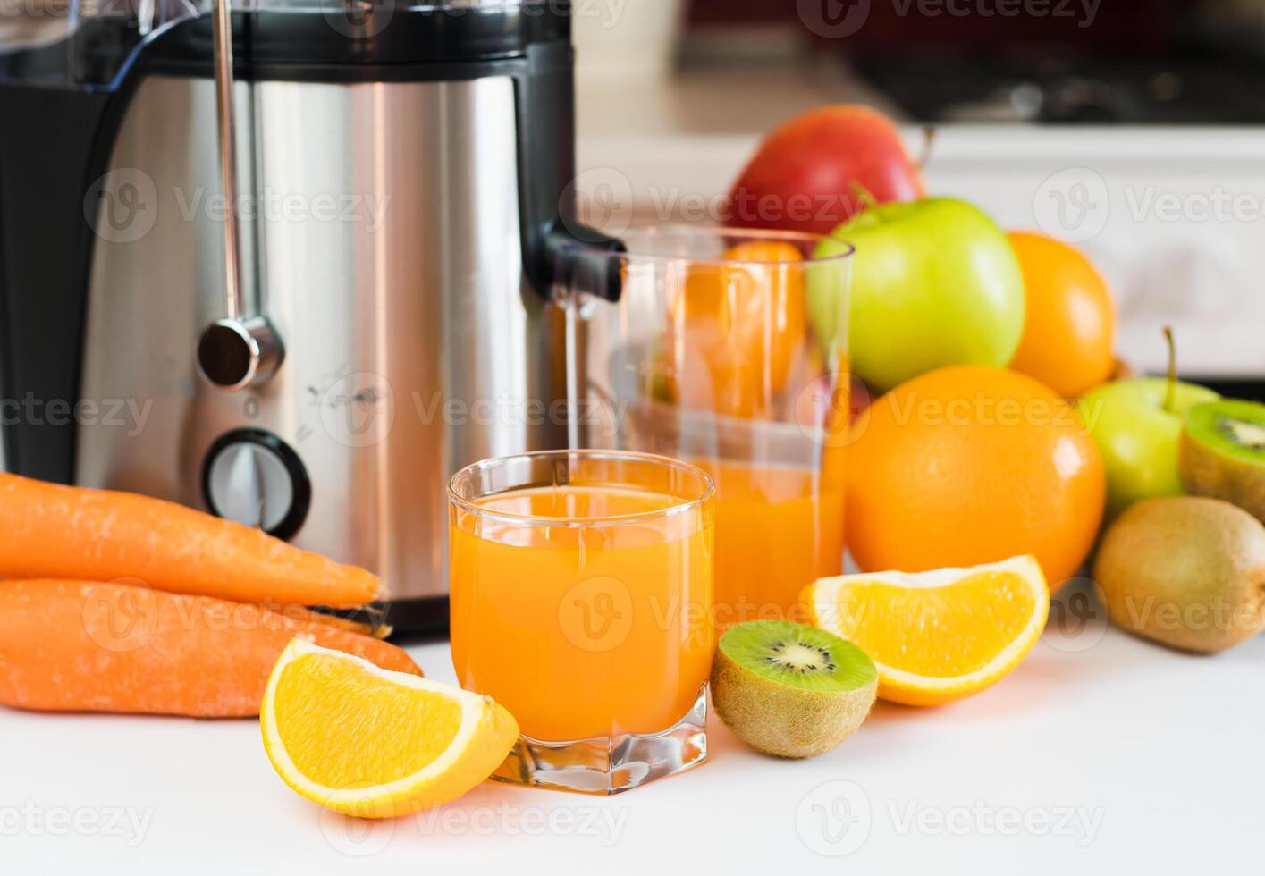 Fresh juice from fruits and vegetables in a glass and modern juicer on the table in the kitchen. Delicious and healthy juices at home. Selective focus. Close-up. photo