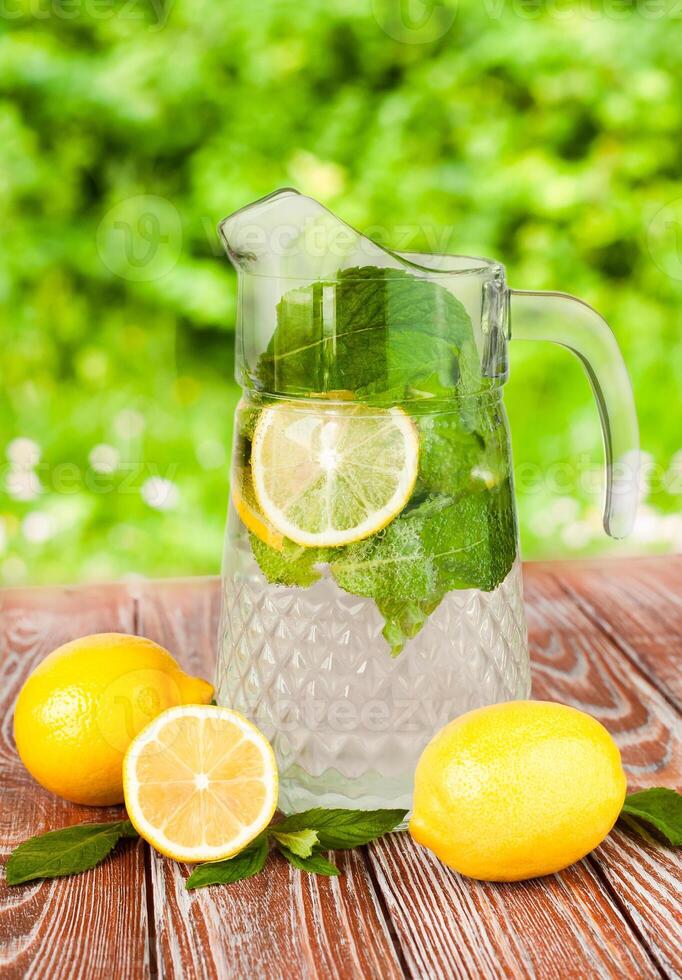 Natural lemonade with lemons, fresh mint and ice cubes on wooden table outdoor. A cool refreshing cocktail in the heat of summer. photo