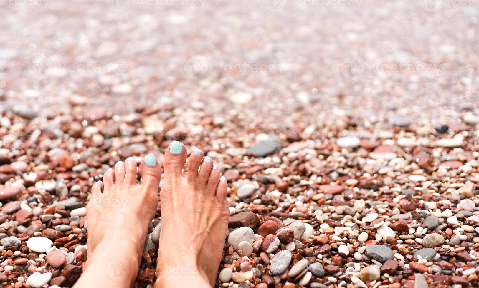 Woman's feet on a pebble beach on the sea. Vacation and travel concept. Rest, relaxation, sunbathing. Close-up. Copy space. Selective focus. photo