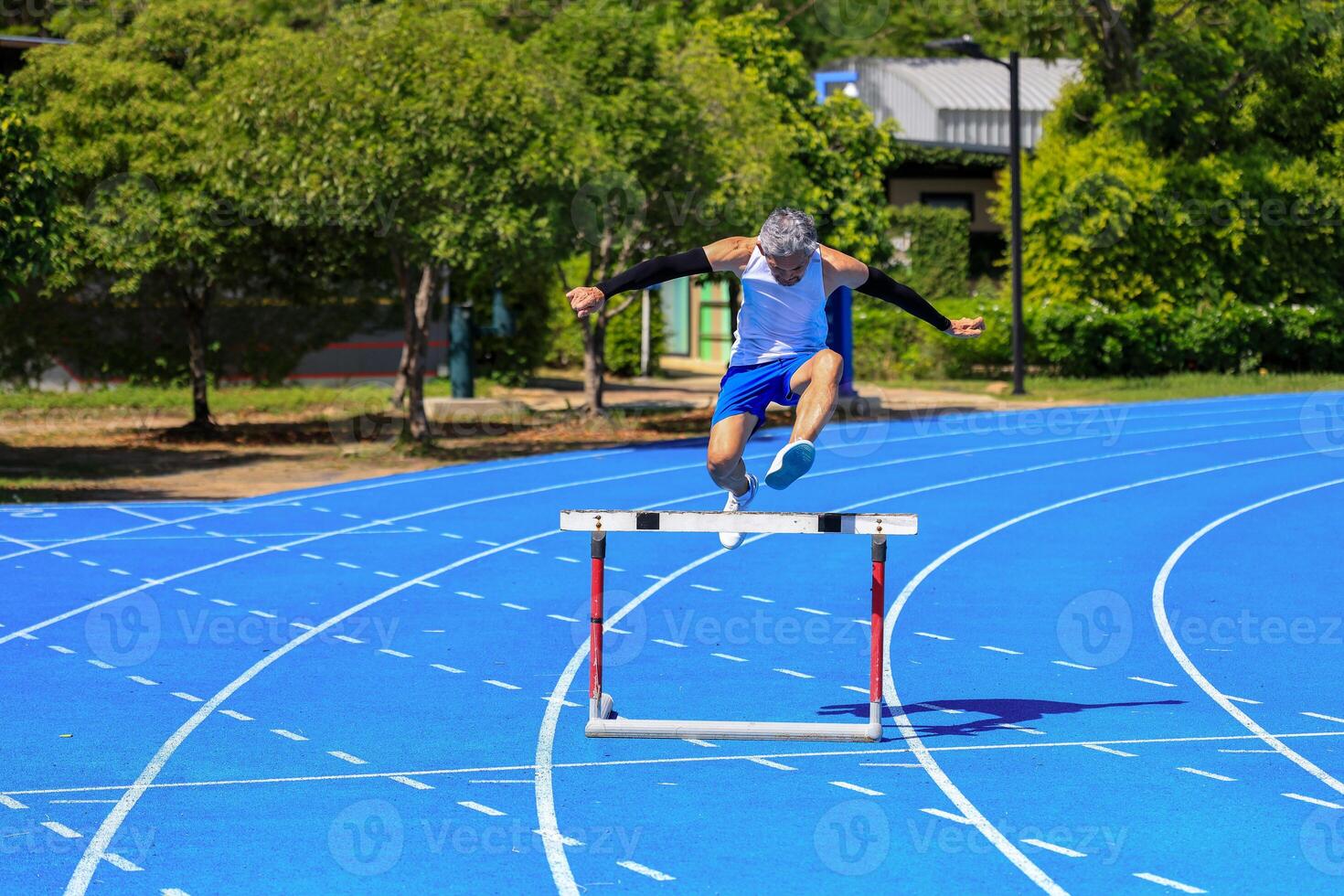 Senior Asian athlete is practicing hurdling running in the professional blue track for professional exercise, sport training workout and healthy for longevity photo