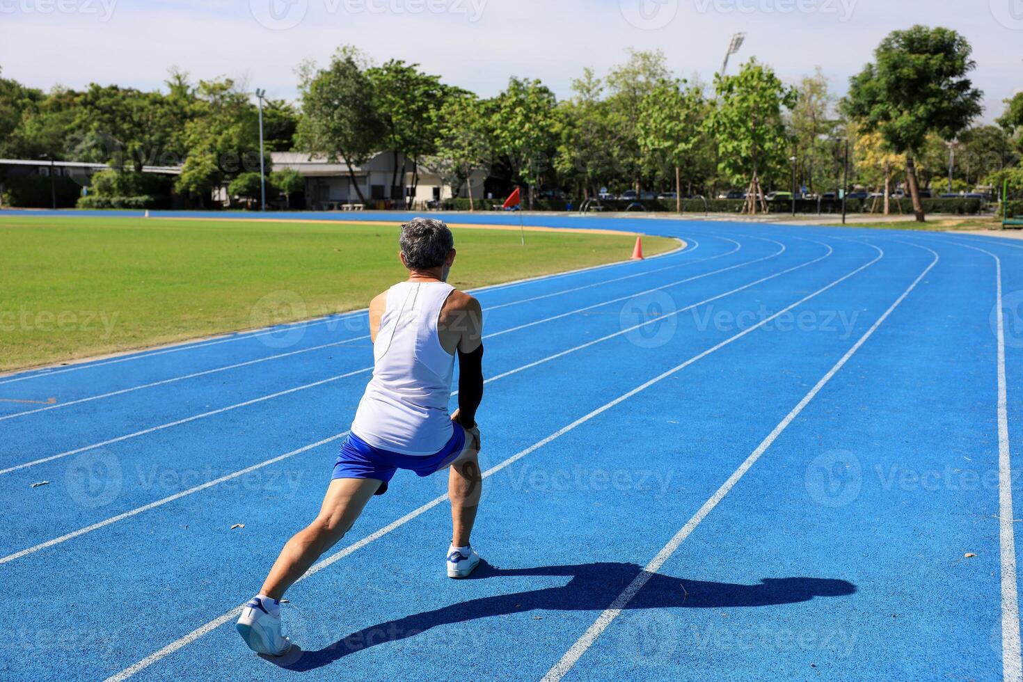 Senior Asian athlete doing stretching warm up for running in the professional blue track for professional exercise, sport training workout and healthy for longevity concept photo