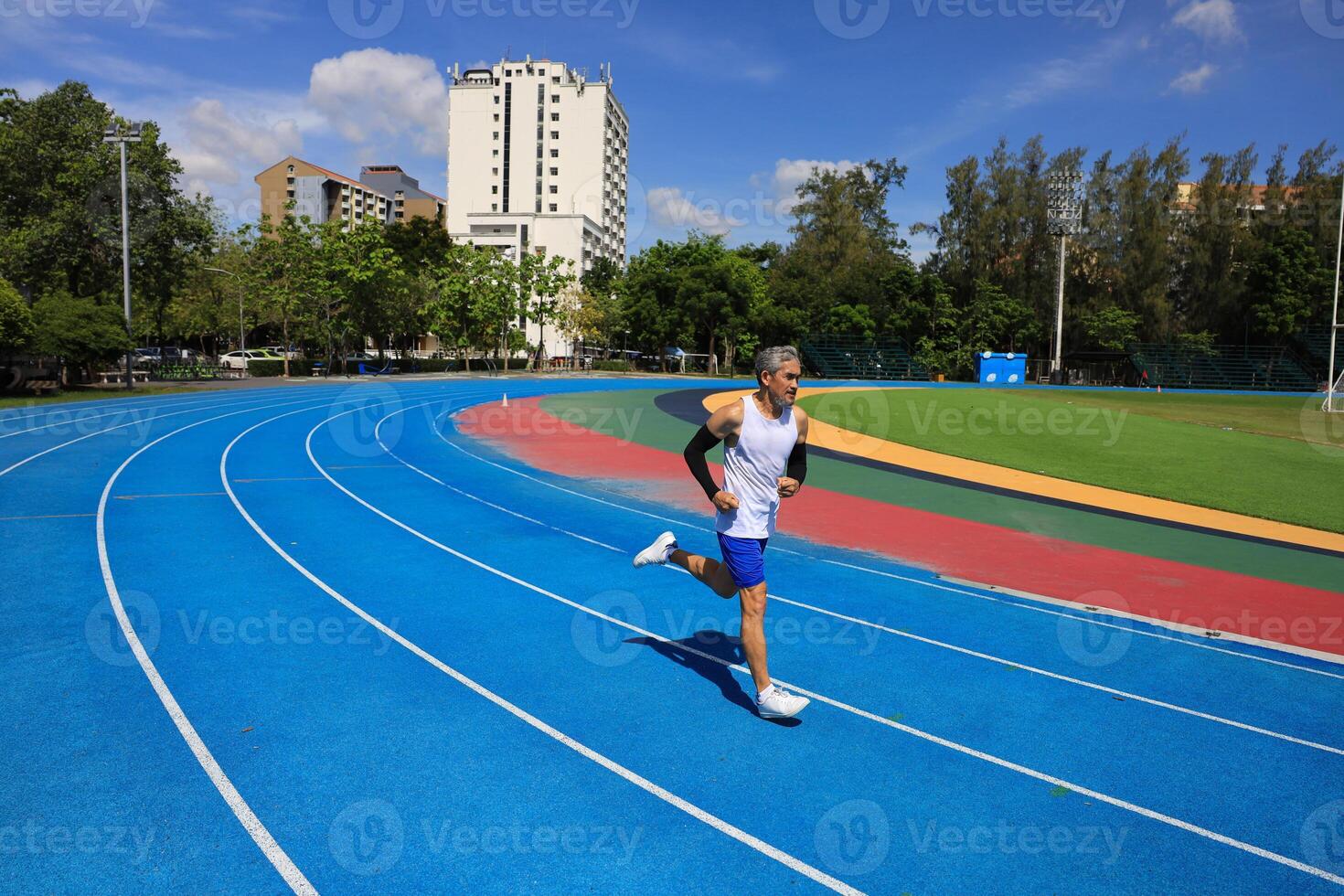 Senior Asian athlete is practicing running in the professional blue track for professional exercise, sport training workout and healthy for longevity concept photo