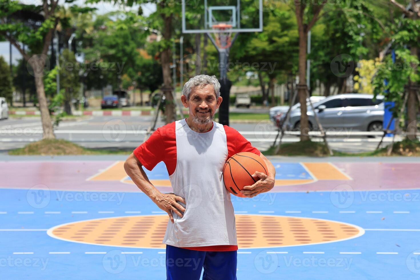 Portrait of senior Asian man in retirement age is playing basketball at outdoor court for healthy and fun activity to exercise and workout against aging illness photo