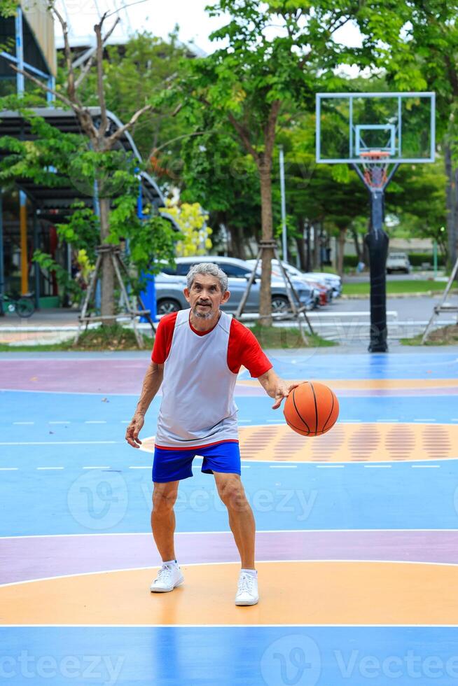 Senior Asian man in retirement age is playing basketball at outdoor court for healthy and fun activity to exercise and workout against aging illness photo