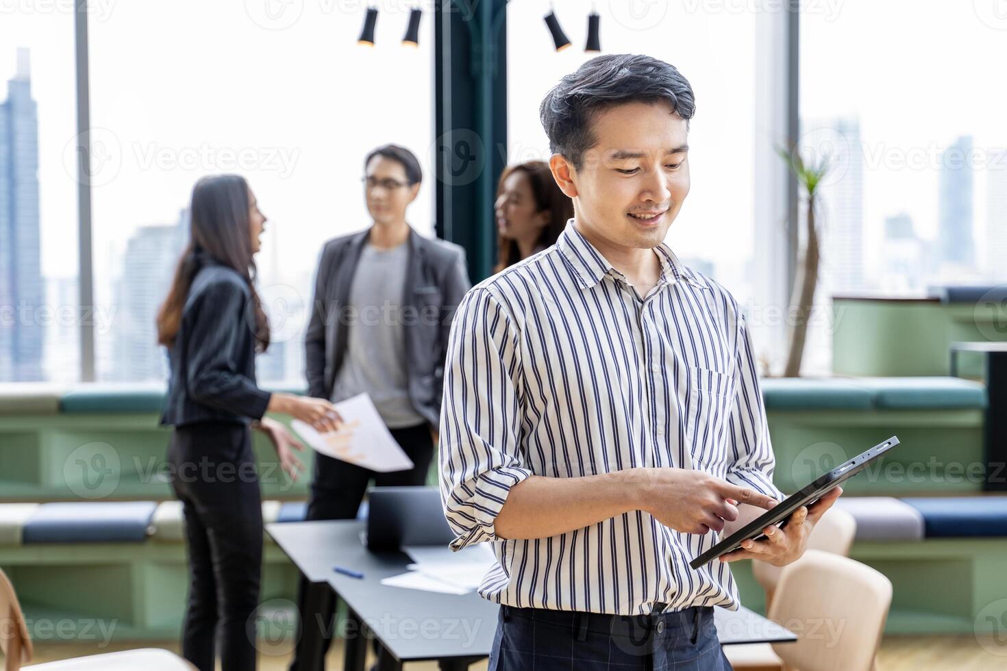Portrait of young Asian businessman smiling with team having small meeting on the back while working in modern co-working space workplace for business and education concept photo