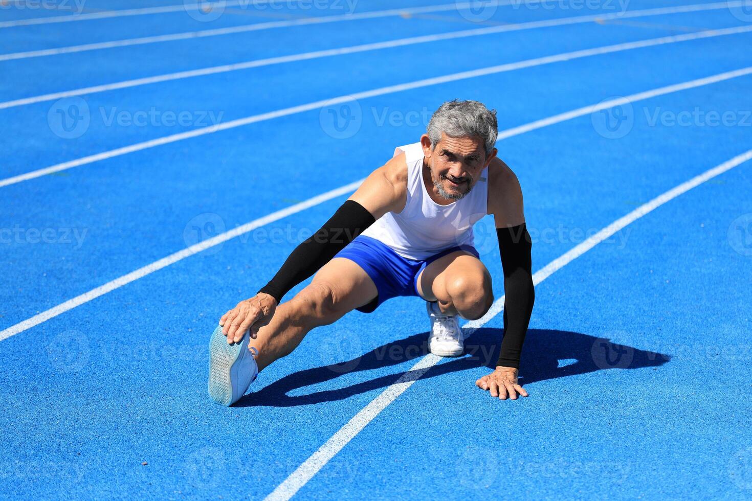 Senior Asian athlete doing stretching warm up for running in the professional blue track for professional exercise, sport training workout and healthy for longevity concept photo