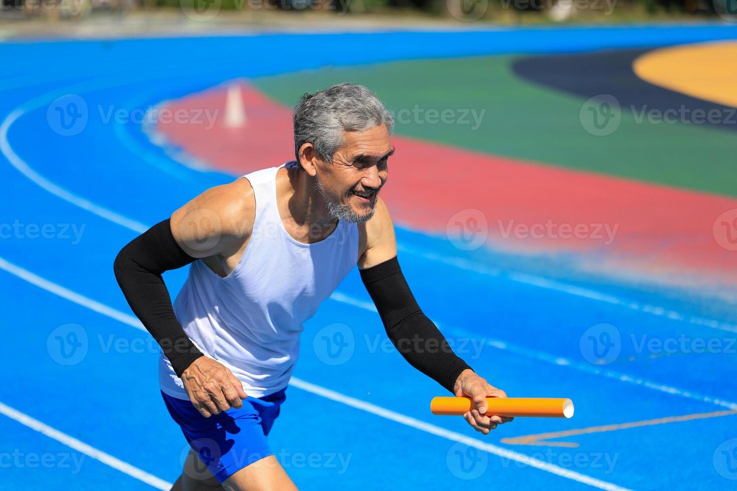 Senior Asian athlete is practicing running with relay baton in the professional blue track for professional exercise, sport training workout and healthy for longevity concept photo
