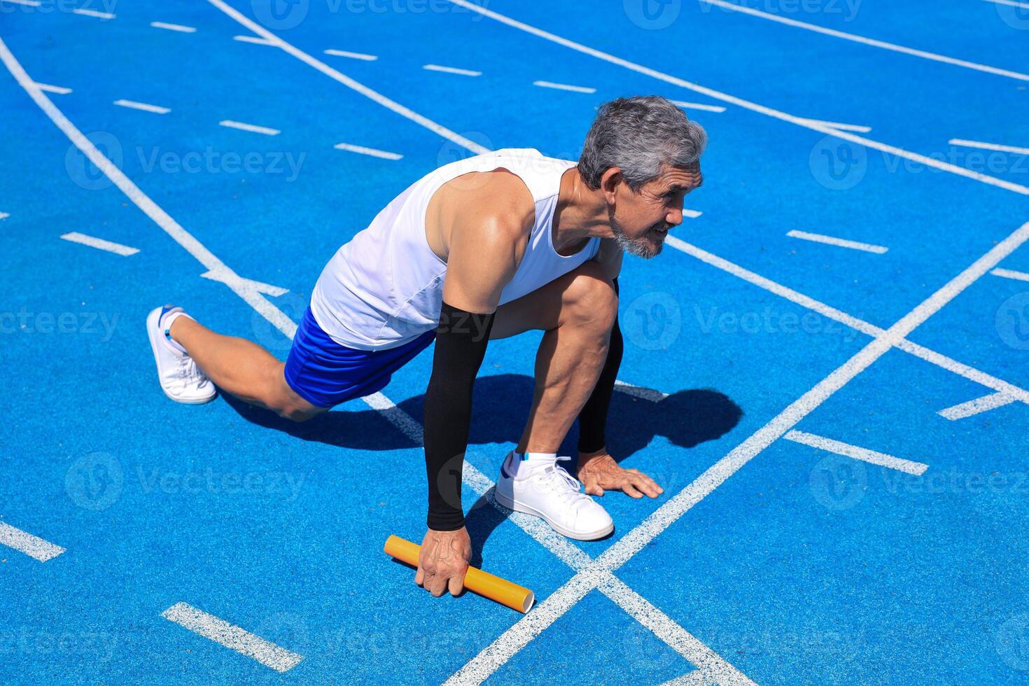 Senior Asian athlete is practicing running block start in the professional blue track for professional exercise, sport training workout and healthy for longevity photo