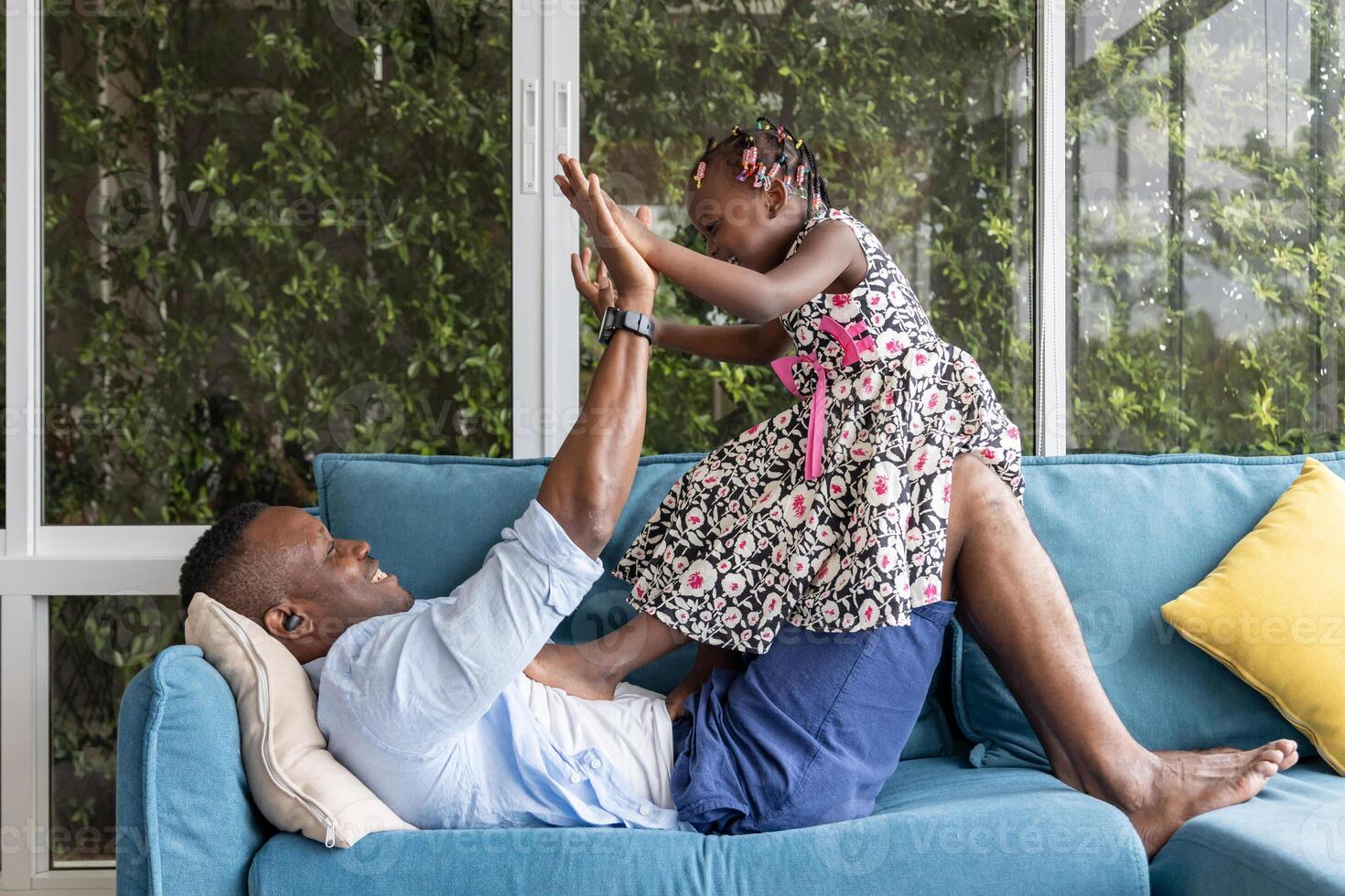 African American father playing with his little daughter as they staying in the sofa couch and spending happy time together at home on the weekend photo