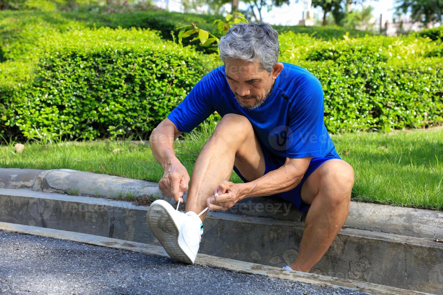 Senior Asian man is tying knot on his running trainer in the morning jogging exercise for healthy and work out photo