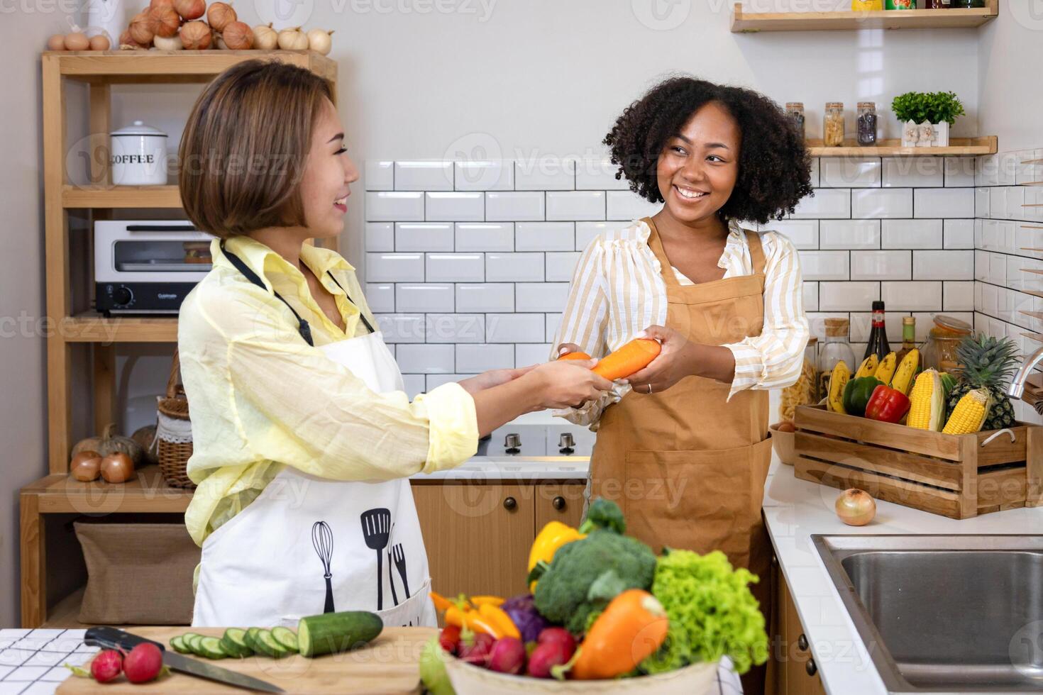 Asian woman and her African American friend is helping each other preparing healthy food with variety of vegetable while washing and cutting the ingredient photo