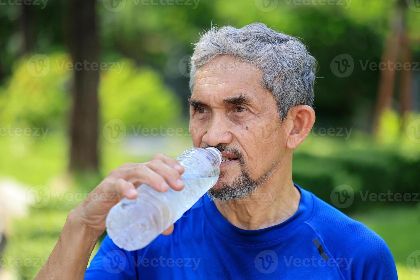 Senior Asian man is drinking water after morning exercise in the park for rehydration of sweat loss and healthy longevity lifestyle photo