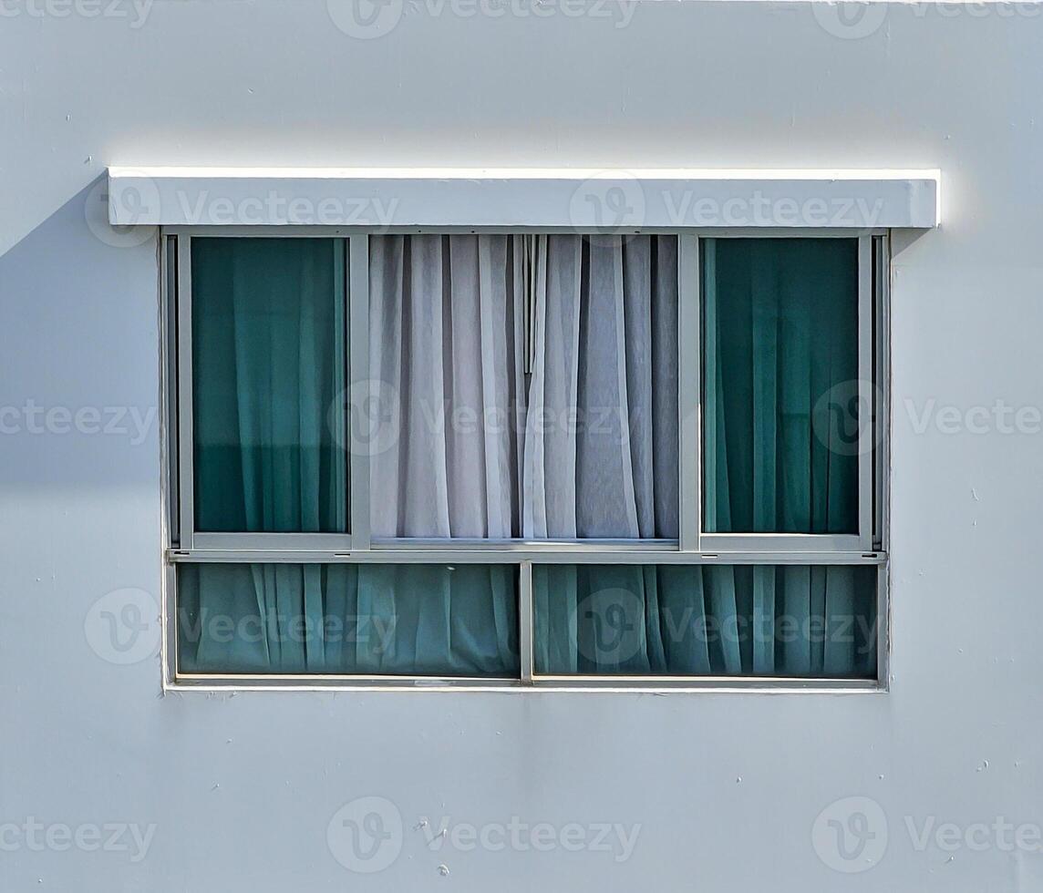 window set in a gray wall, featuring two glass panes with a metallic frame. Light gray curtains of a sheer fabric are partially drawn behind the glass, obscuring the view inside. Design photo