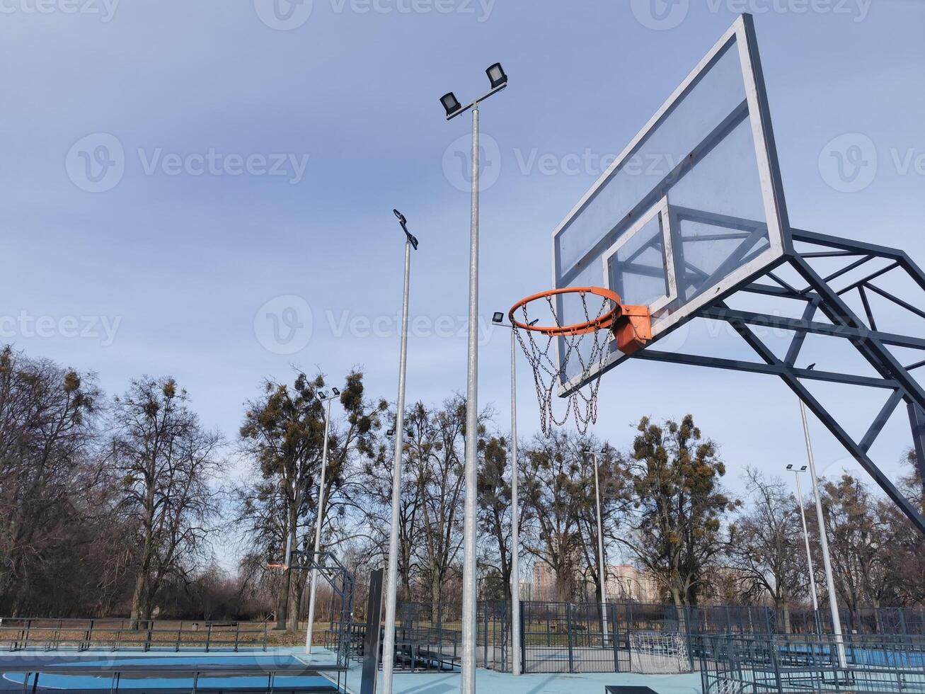 A basketball net under a cloudy sky. The back board has been busted and is now covered with a large piece of wood. photo