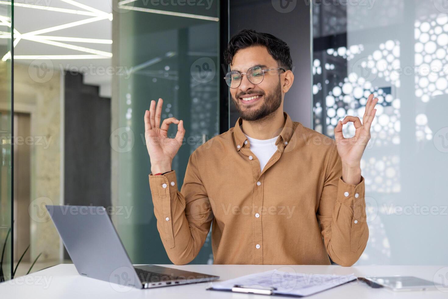 Young professional practicing yoga at his work desk in a modern office setting, showcasing relaxation and mental wellness. photo
