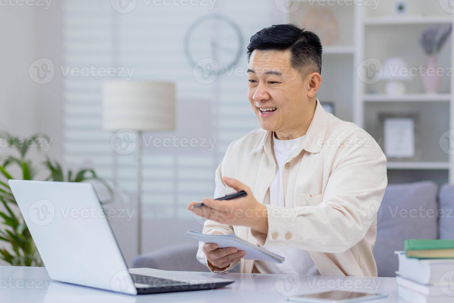Asian man interacts with a webinar on his laptop at home, expressing happiness and engagement. This image captures the joy of lifelong learning and the convenience of online education. photo
