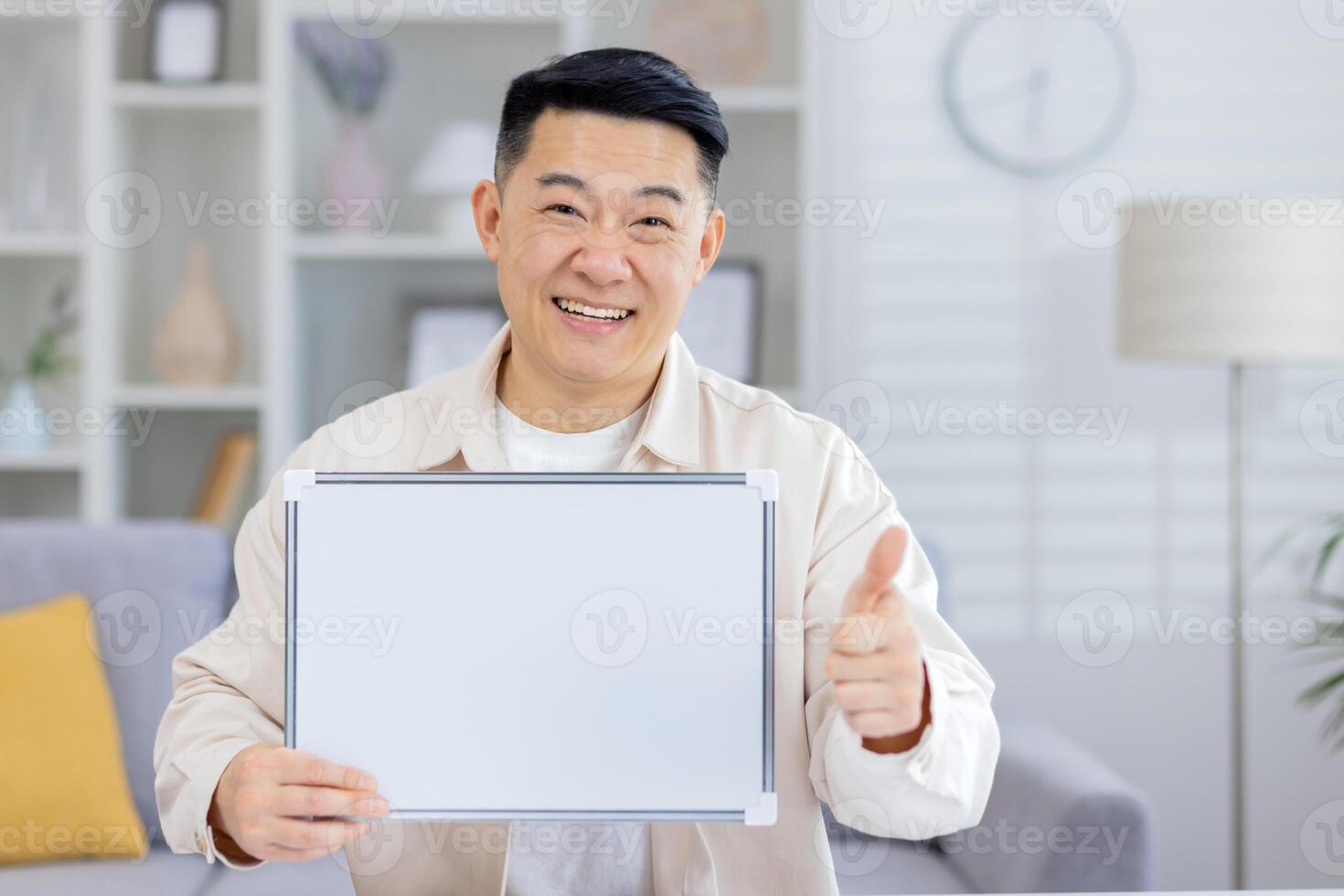 Cheerful man presenting a blank whiteboard and showing a thumbs up gesture while standing in a bright, modern living room setting photo