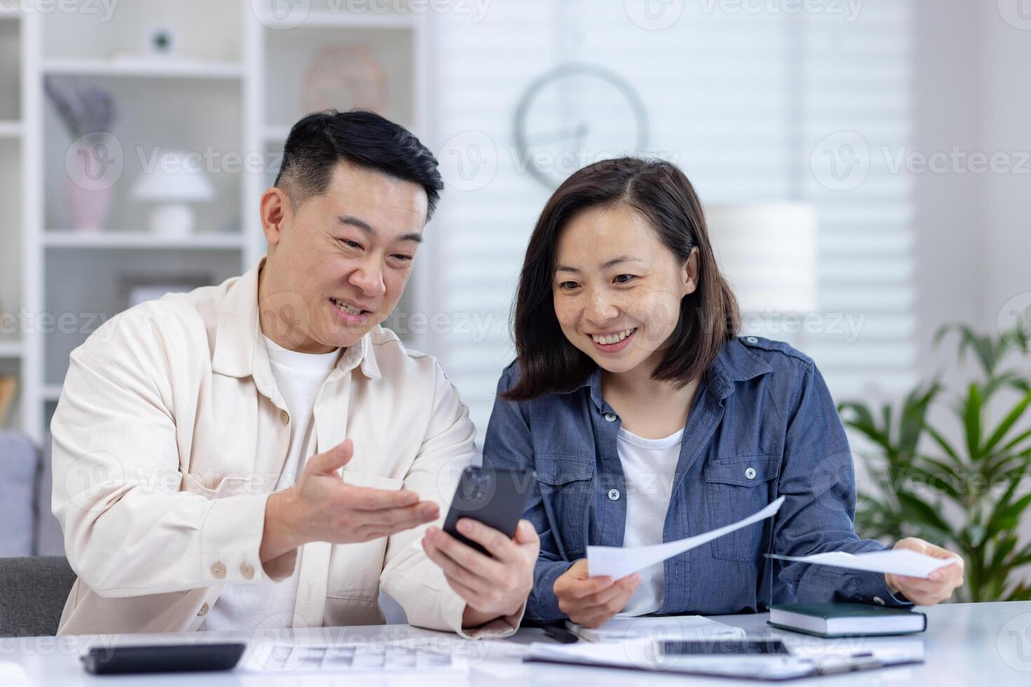 Smiling couple reviewing financial documents and using smartphone at home, demonstrating teamwork and financial planning photo