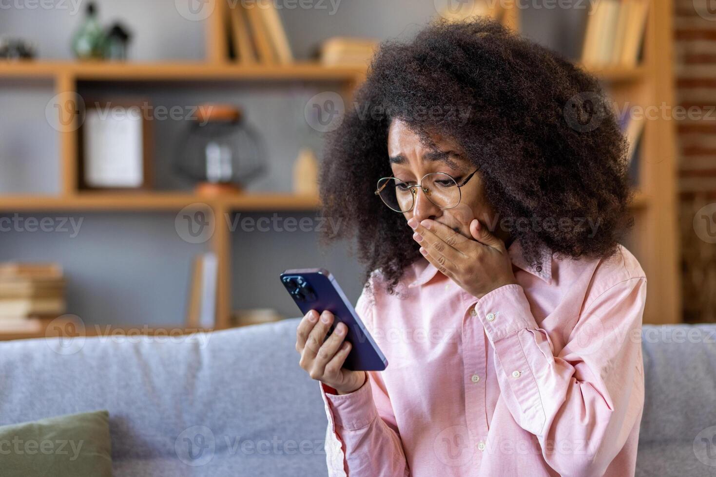 Sad disappointed woman received breaking news on phone, african american woman reading bad news online using app on smartphone, sitting at home on sofa in living room of house. photo