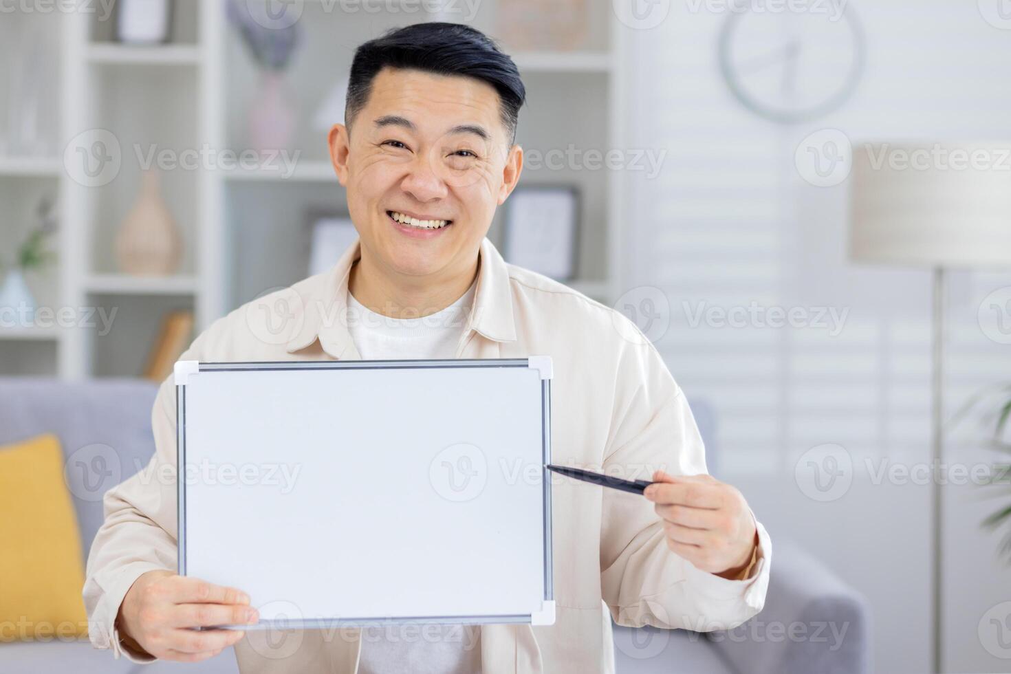 Happy man showcasing a blank whiteboard in a comfortable living room setting while holding a pen. photo