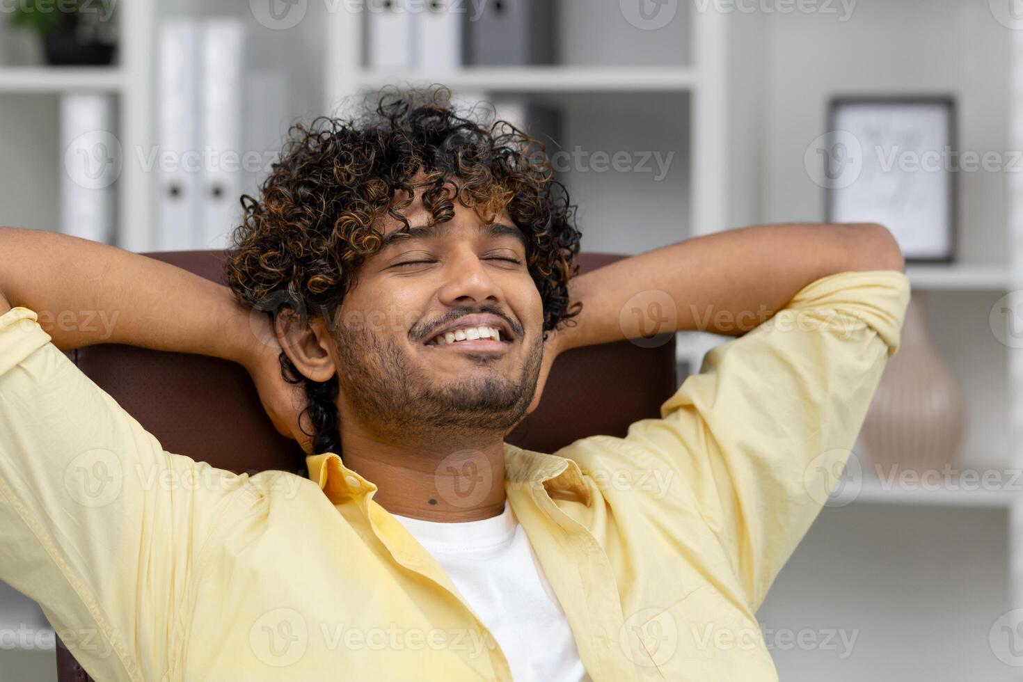 Man sitting at a desk with closed eyes and a relaxed smile, enjoying a moment of calm and peace. photo