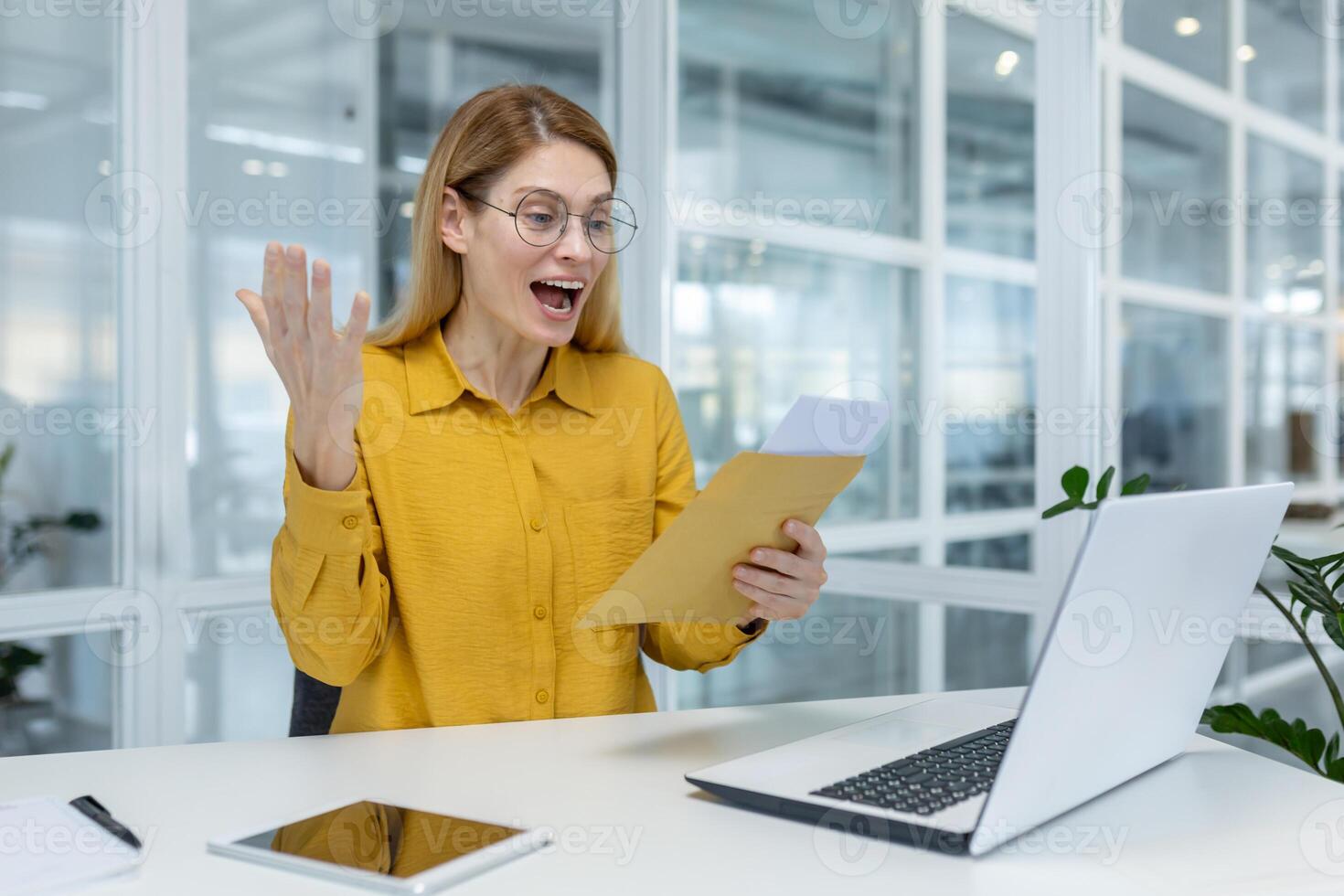 A joyful woman is delighted by positive news received through the mail while working with her laptop in an office setting. photo