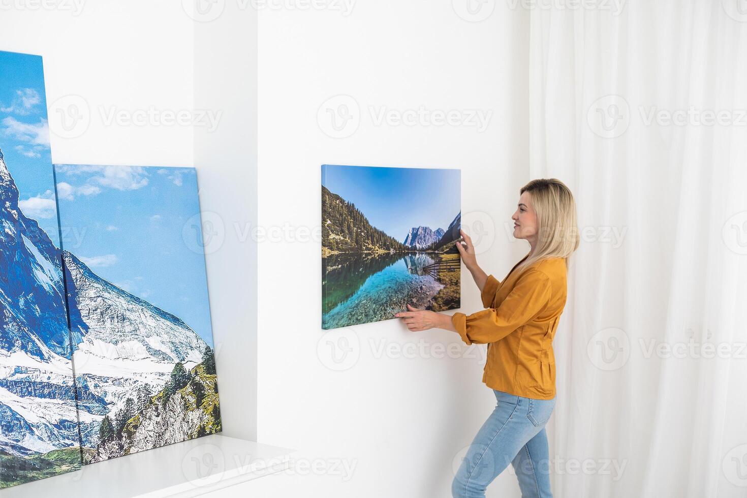 Canvas print with gallery wrap. Woman hangs photography on white wall. Hands holding photo canvas print