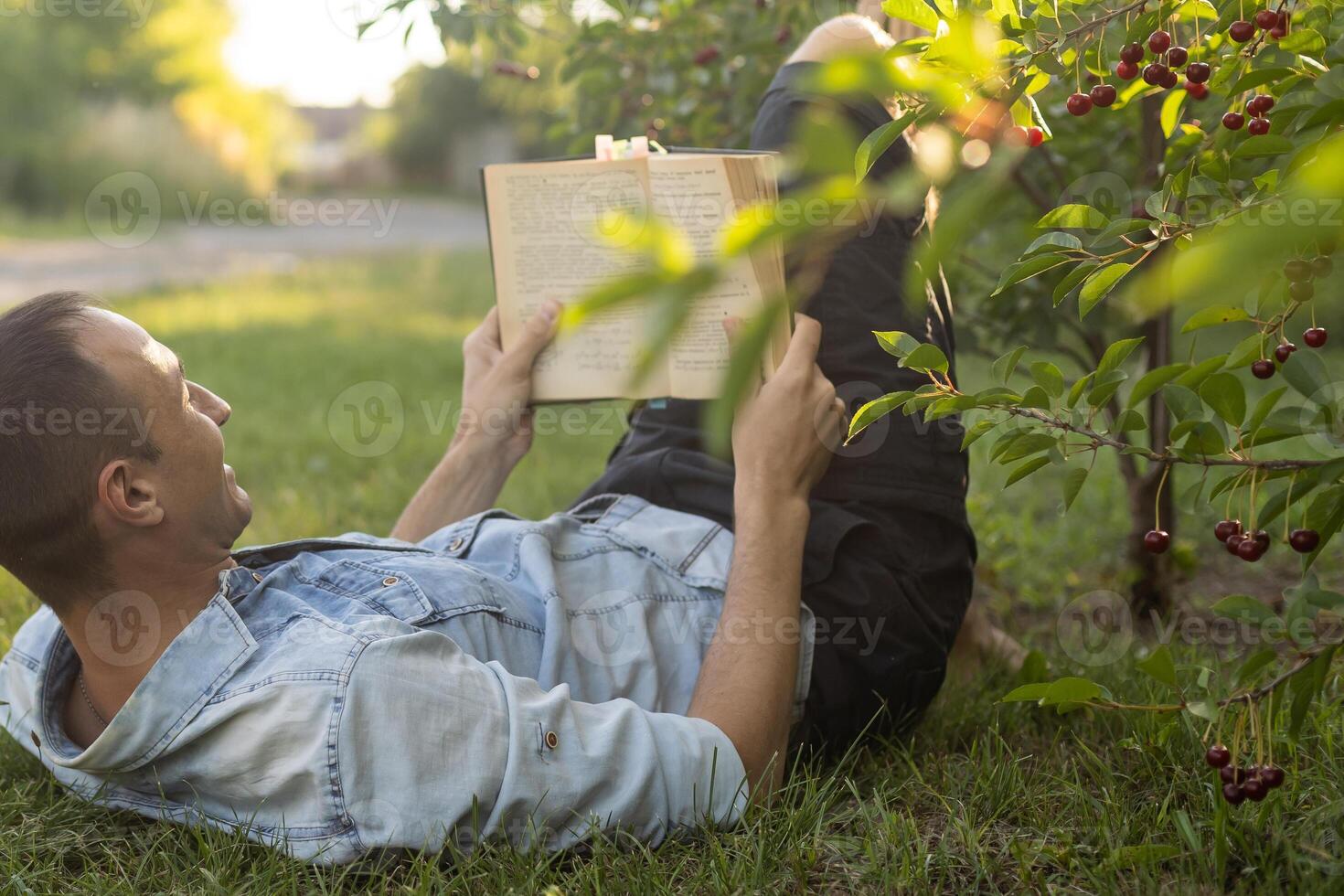 Young man lying in the grass, relaxing and reading a book photo