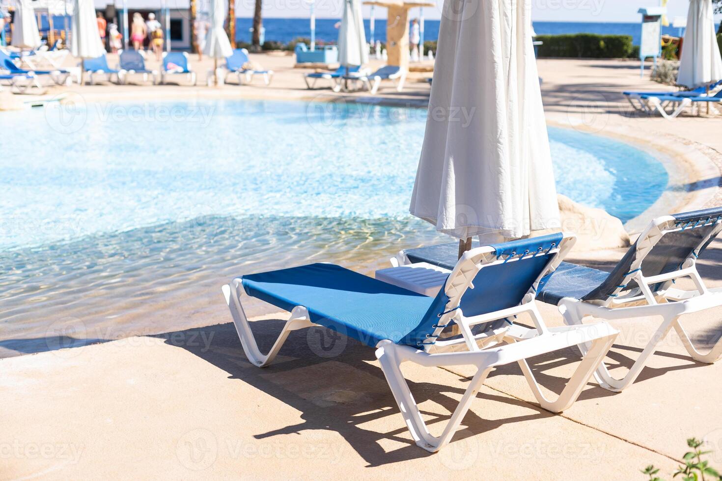 Swimming pool with clean clear water, nobody. Square shaped pool with blue tiles with grab bars ladder and sunbeds on the decks, no people. water surface. Overhead view. Summer background. photo