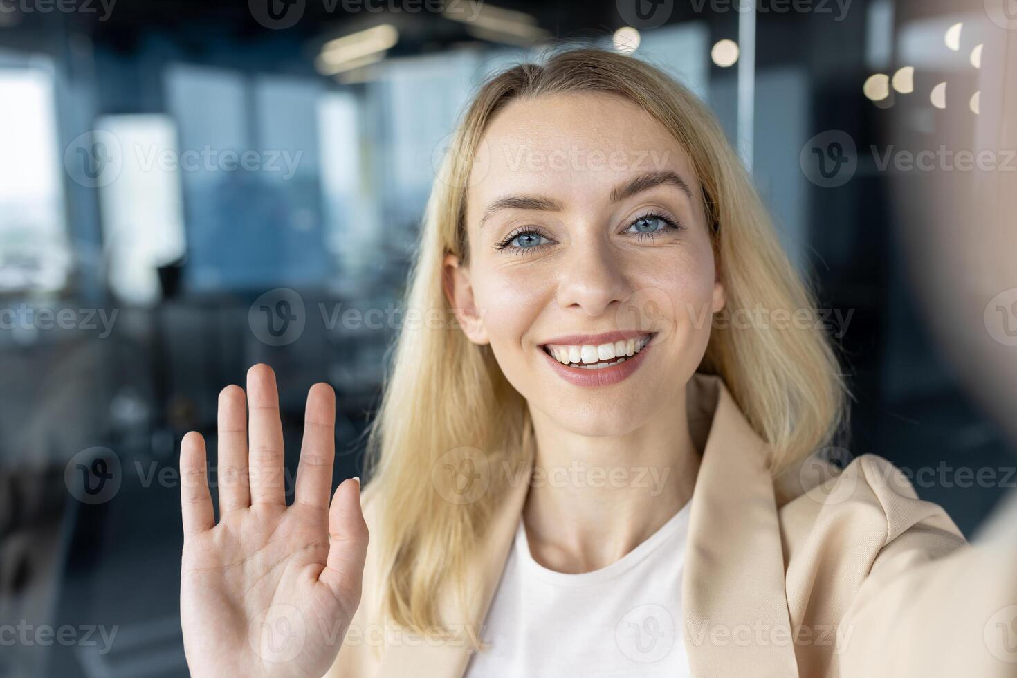 A cheerful young professional woman waving at the camera with a beaming smile in a contemporary office setting. photo