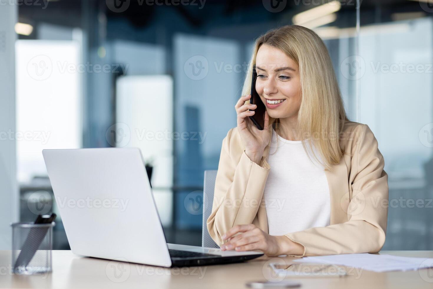 A businesswoman is engaged in conversation on her mobile phone while using a laptop in a modern office environment. photo