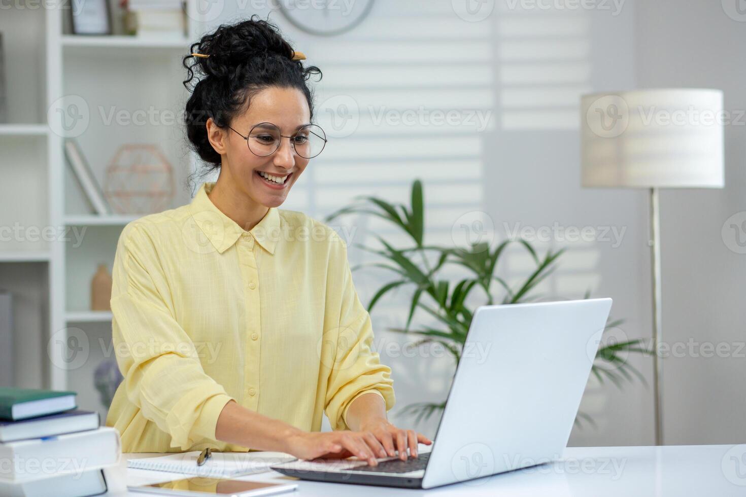 A smiling woman in glasses working on a laptop at a home office desk, capturing a positive and productive atmosphere. photo