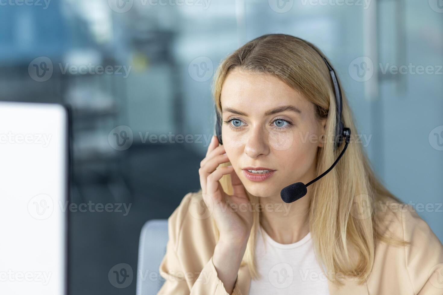 A young professional woman wearing a headset in a modern office setting, focused on a customer service call. She exemplifies competence and attention. photo