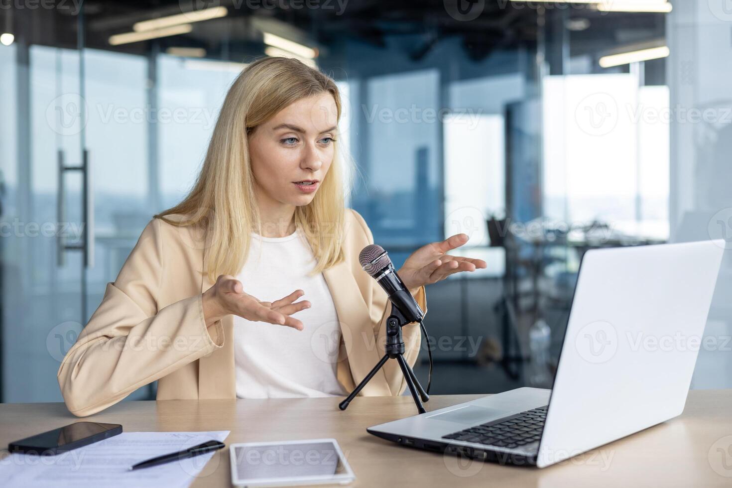 A focused professional woman is speaking into a microphone, explaining concepts during a presentation in a contemporary office setting. Her expression and gestures suggest engagement and clarity. photo