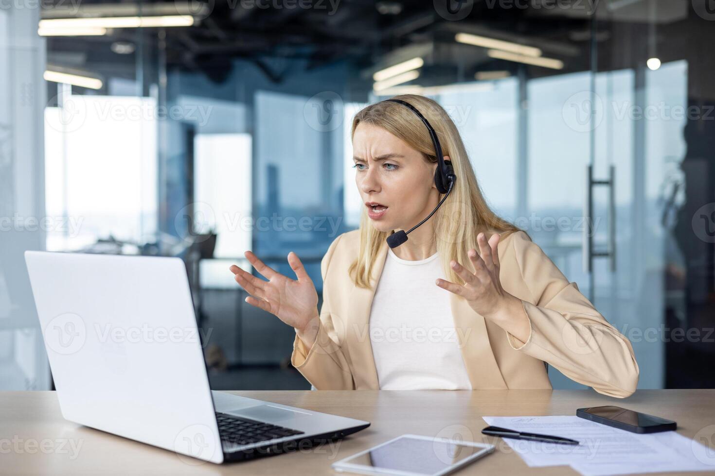 Blonde businesswoman wearing a headset shows frustration while on a call in a modern office setting. Her expression conveys stress and confusion during the virtual meeting. photo